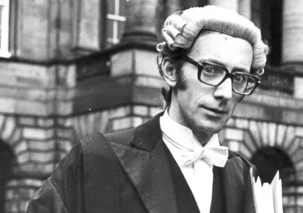 A black and white press photograph of a barrister in wig and gown outside a courthouse.