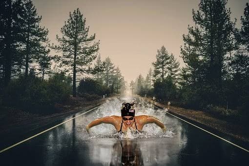 A swimmer front-crawling down the middle of a wet tarmac road.